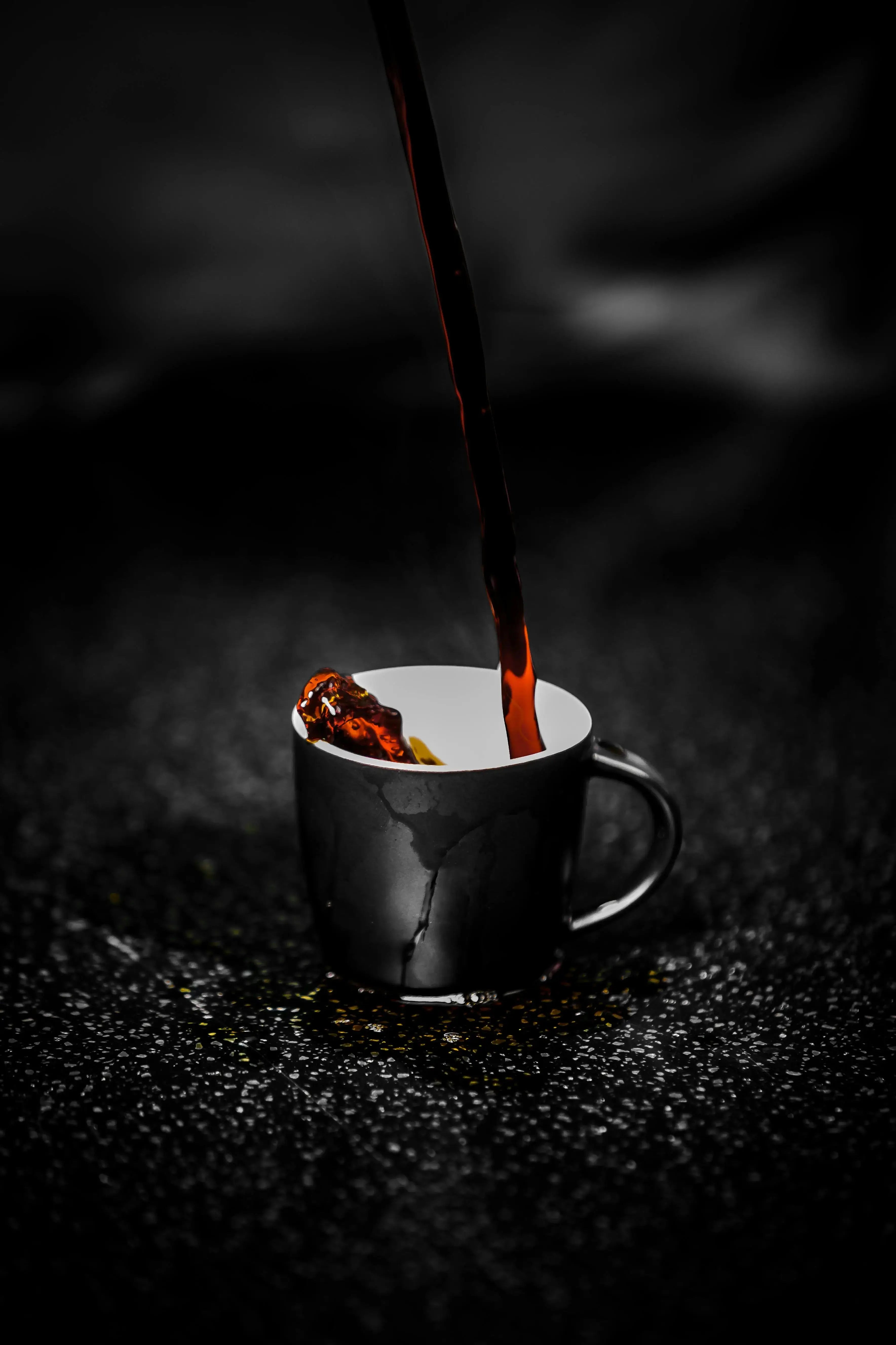 Black cup surrounded by black coffee beans with black coffee pouring into it